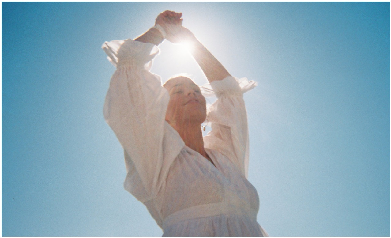 A woman in white silhouetted against the sun and a clear blue sky