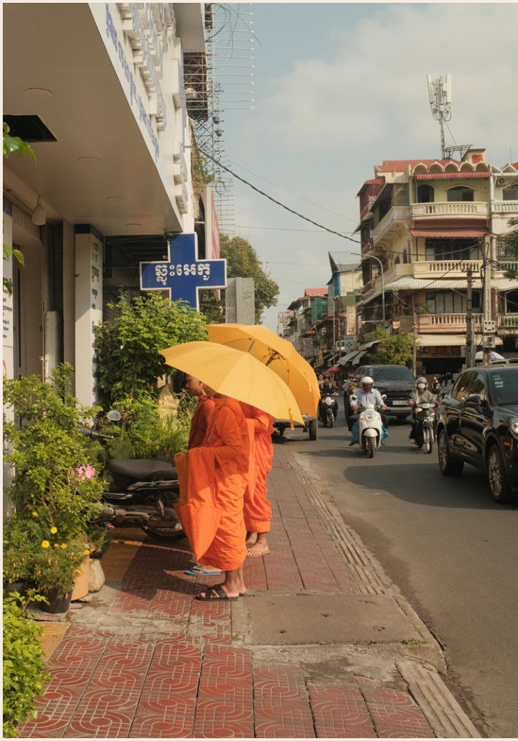 Two monks in orange robes with yellow umbrellas on a street in Cambodia