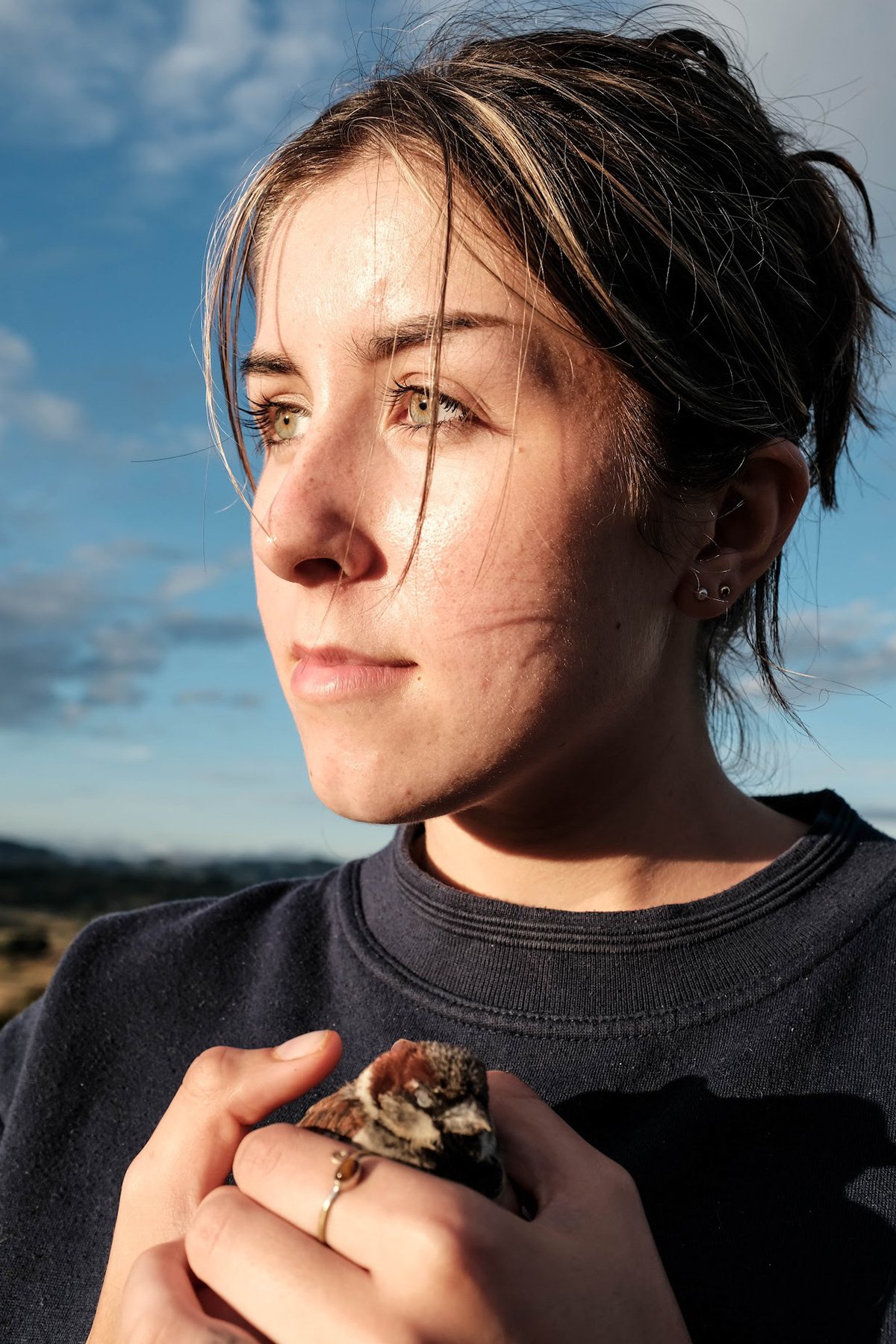 A woman holding a small bird, backlit against the sky