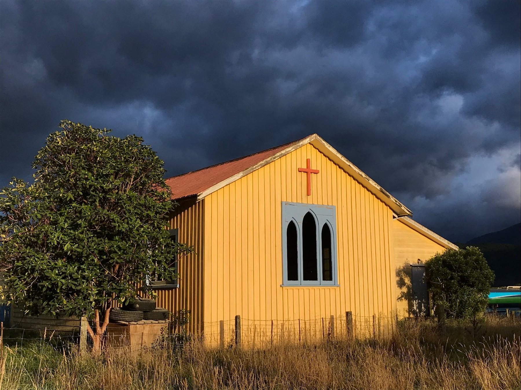 A small yellow wooden church lit by golden light under a dark stormy sky