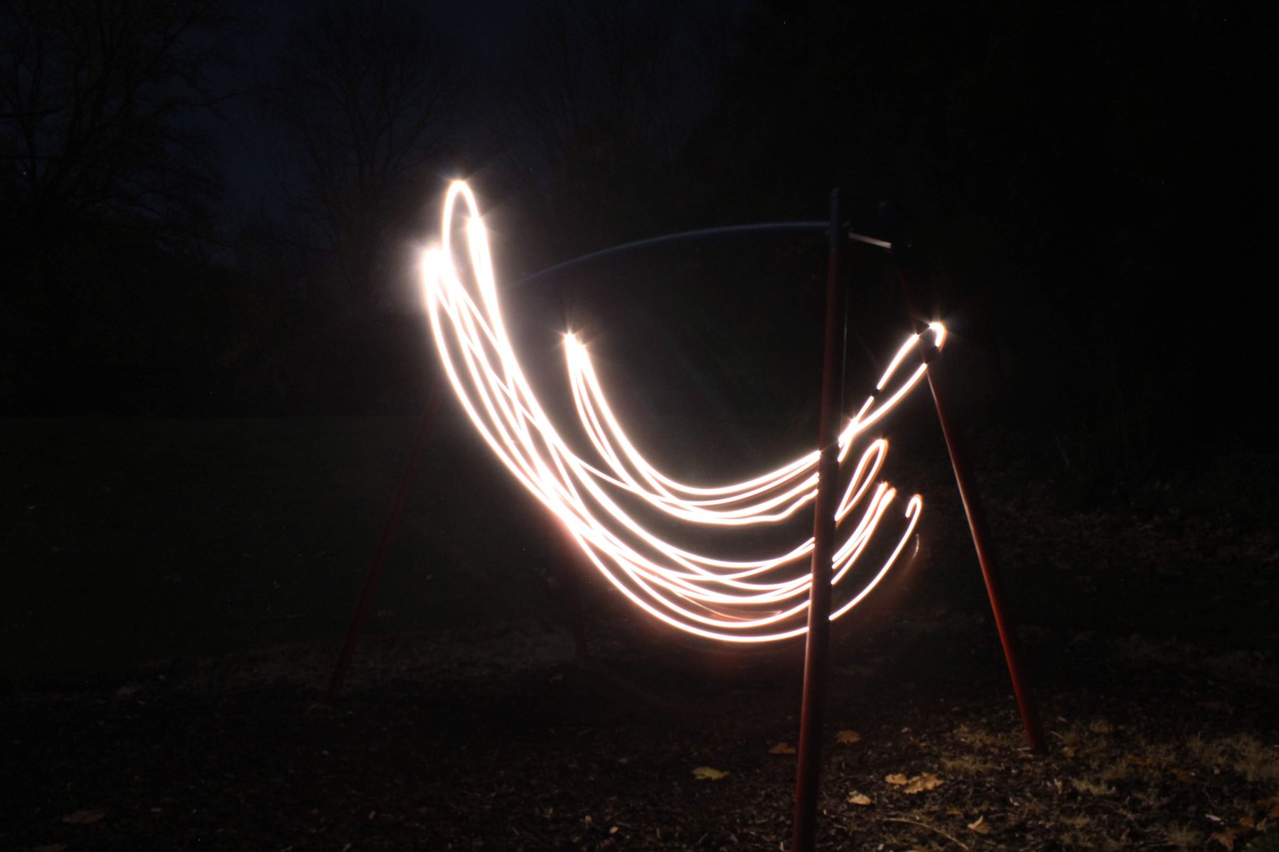 Long-exposure light trails from fireworks over a swing set at night
